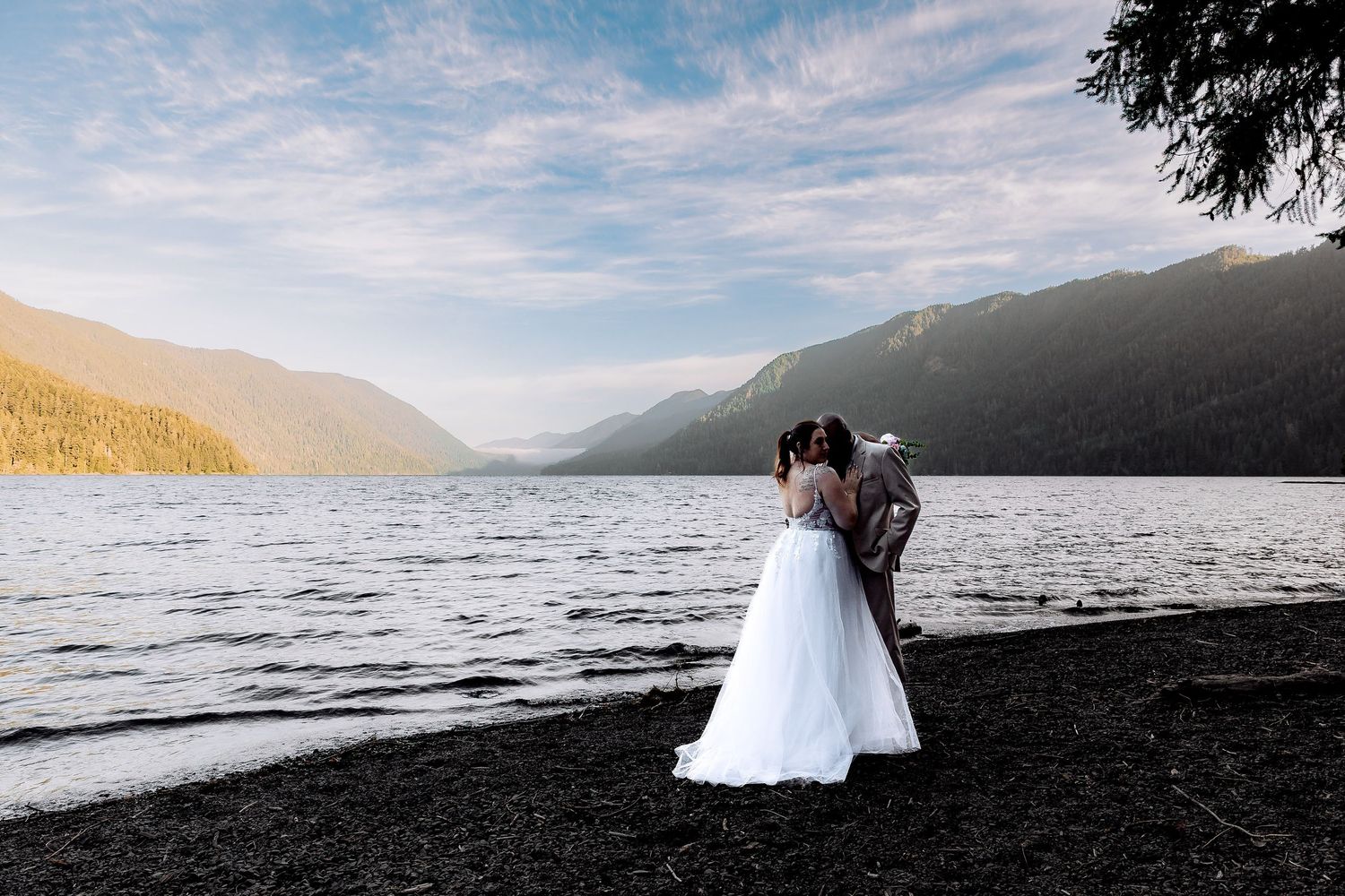 Couple enjoys romantic lakeside moment against mountain backdrop at Lake Crescent with moody cloudy skies.