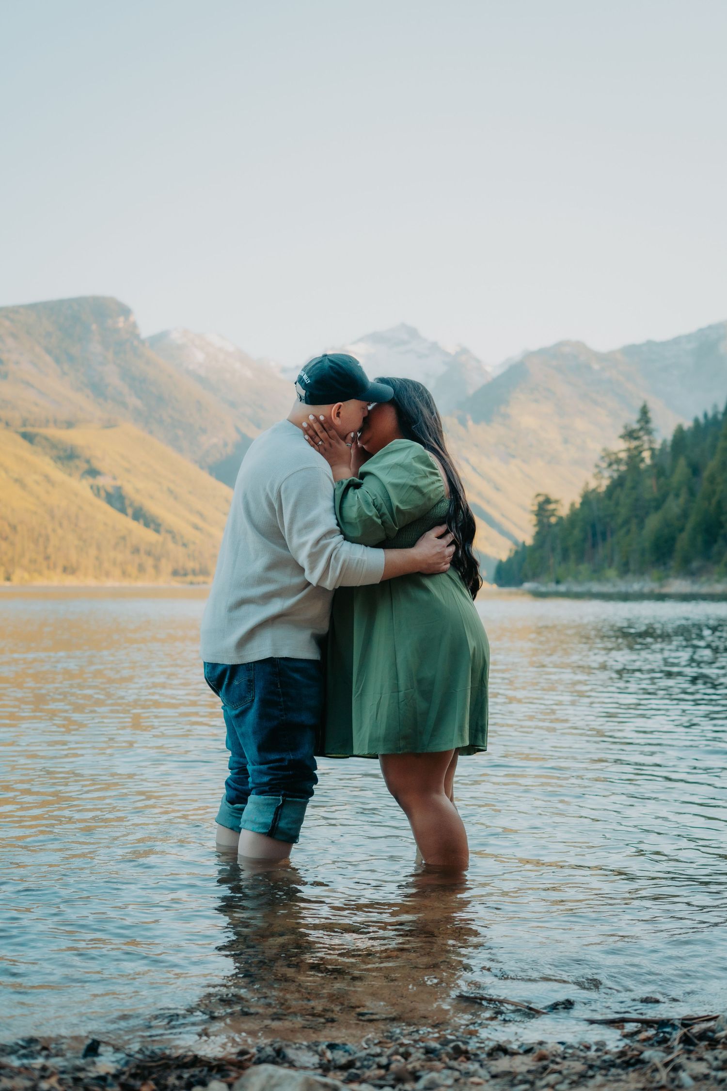 A couple shares an intimate moment while standing in a mountain lake during sunset.