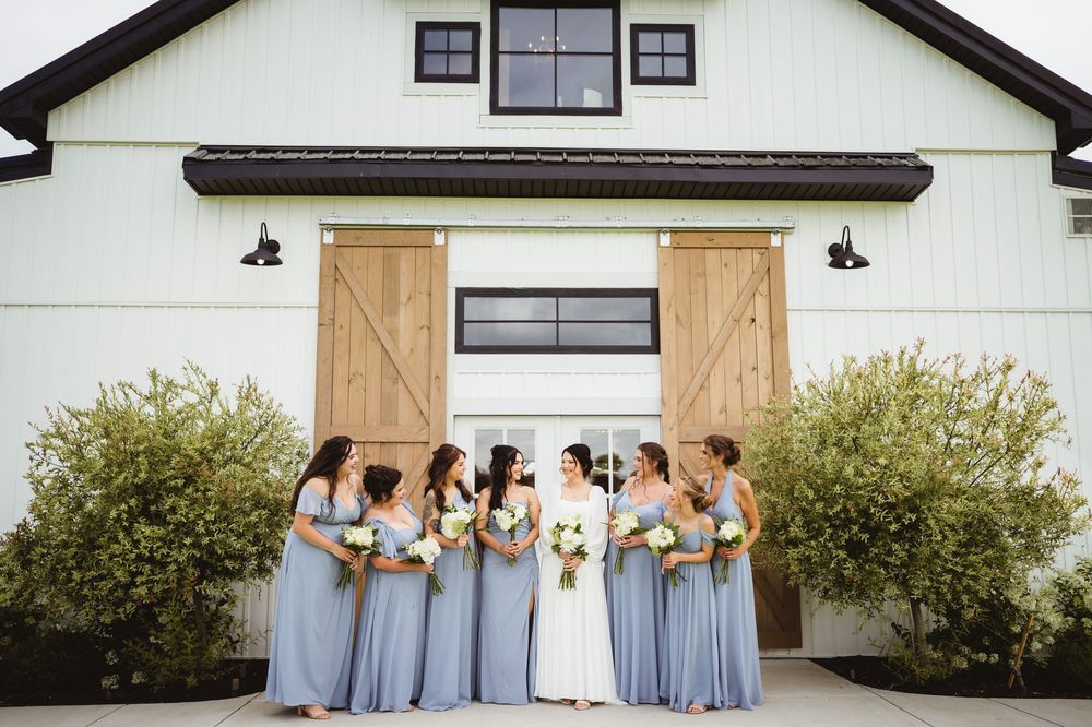 Five bridesmaids in matching light blue dresses laughing together outside a white building with black trim.