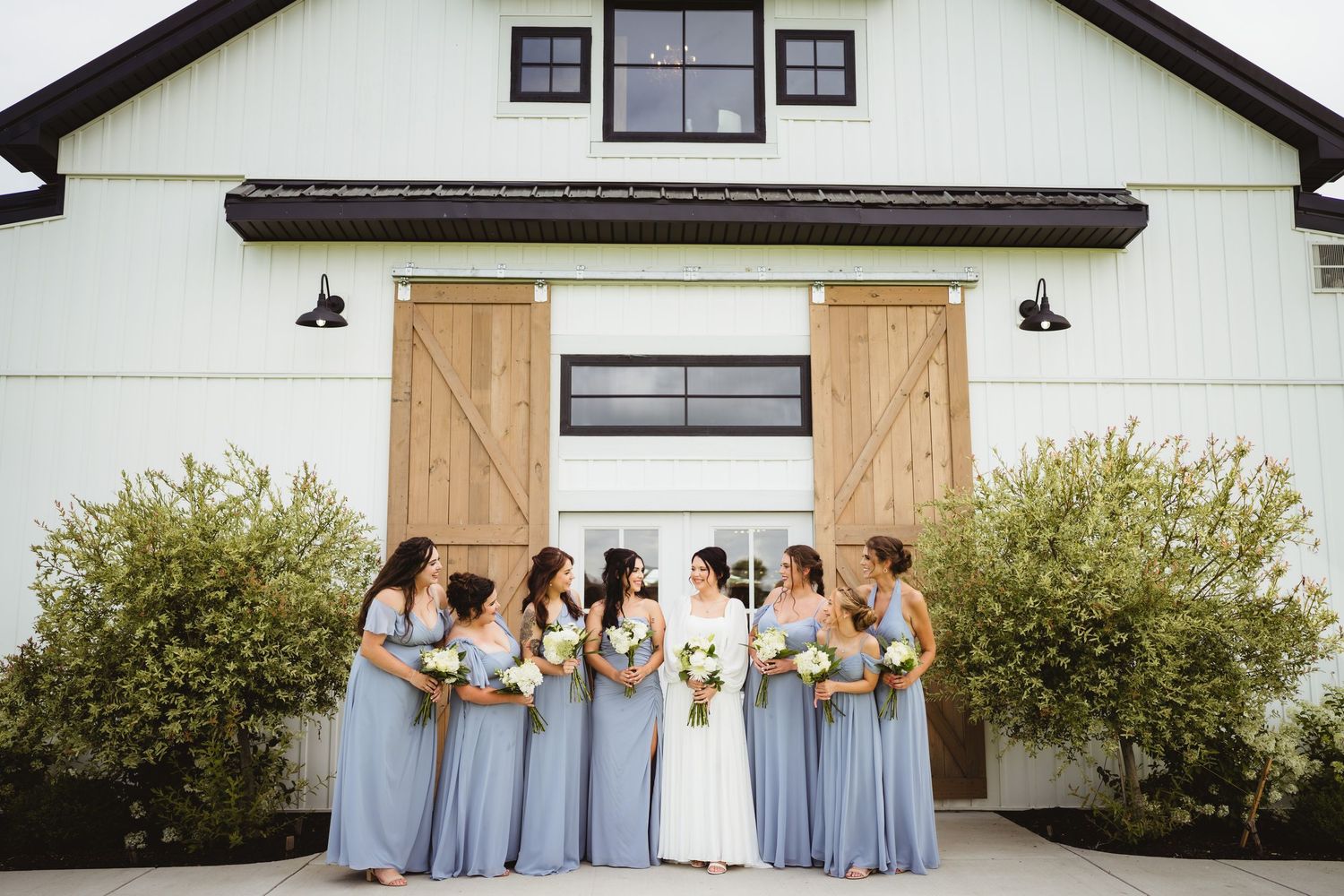 Five bridesmaids in matching light blue dresses laughing together outside a white building with black trim.