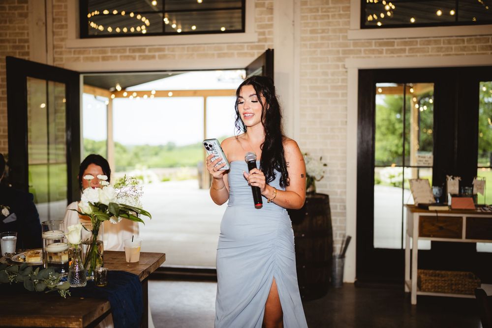 Someone in a light blue dress gives an emotional speech at an elegant indoor venue with brick walls and large windows.