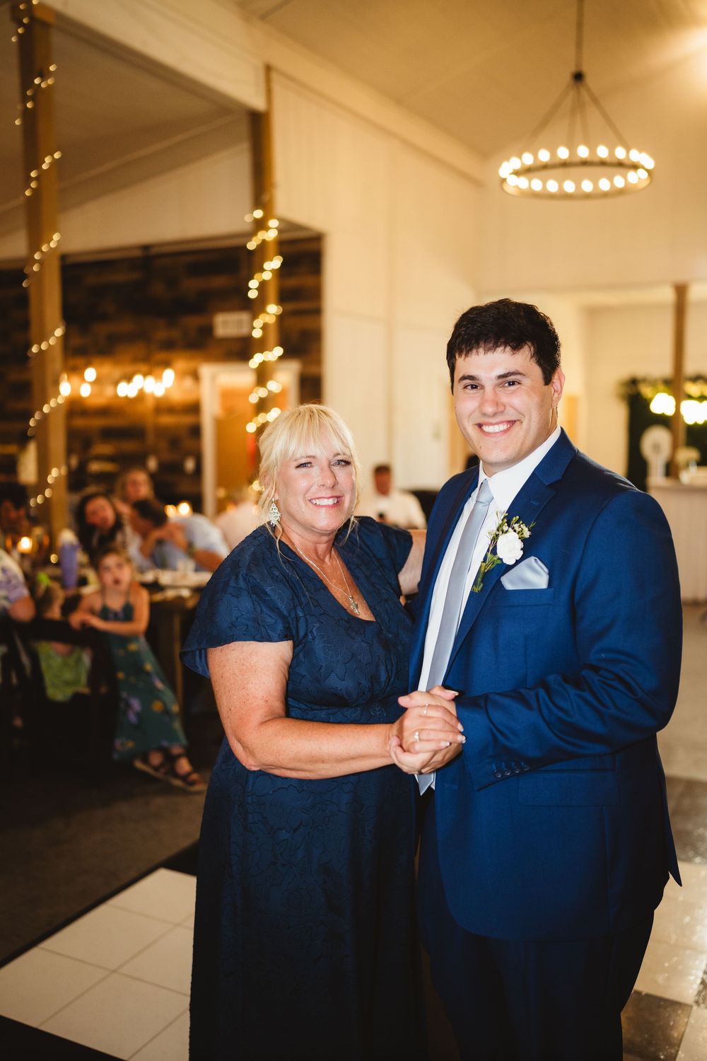 A couple dances together at a wedding reception in a beautifully lit venue with chandeliers overhead.