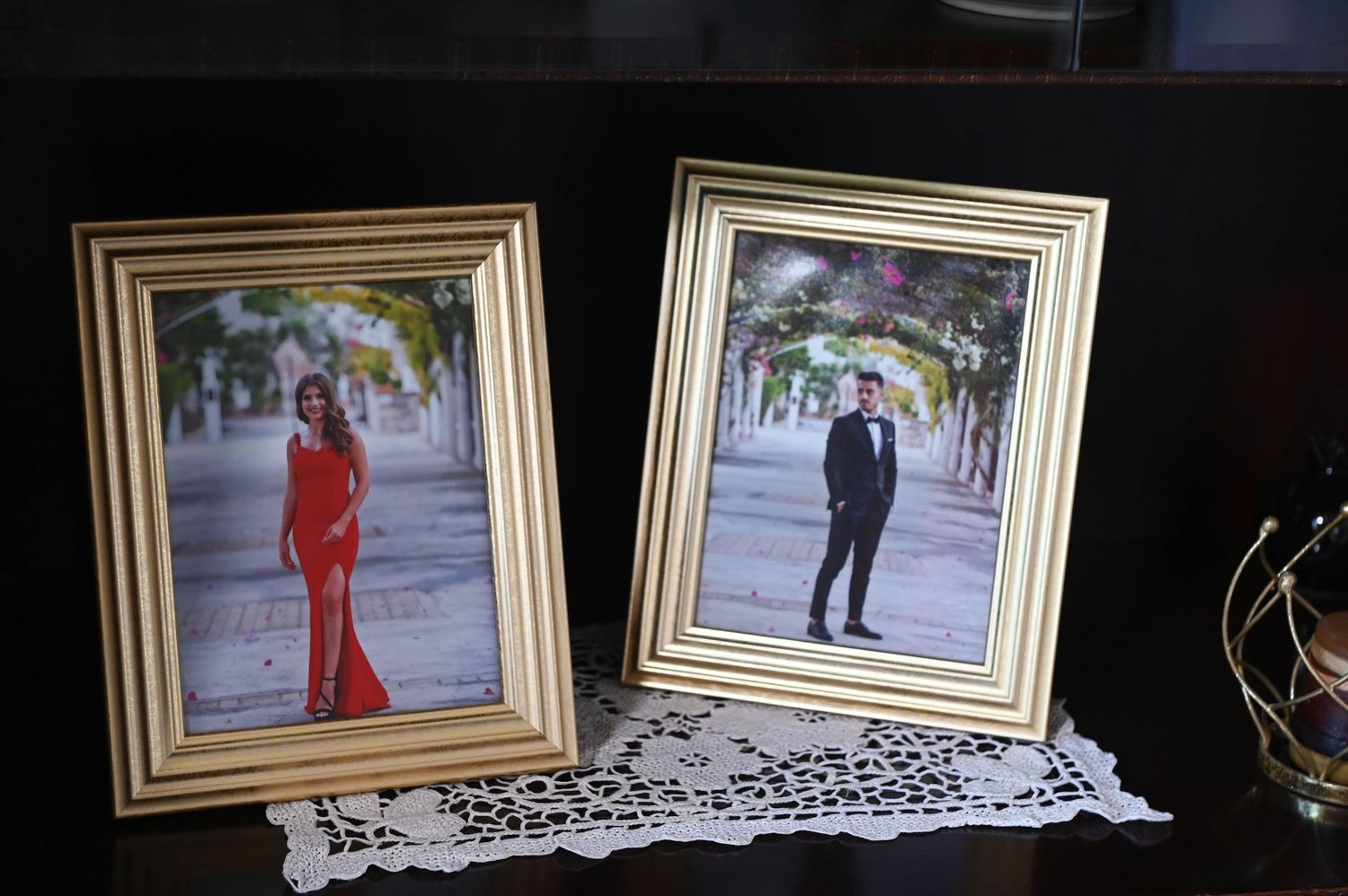 Two framed photographs on a lace doily show formal portraits featuring individuals in red and black attire.