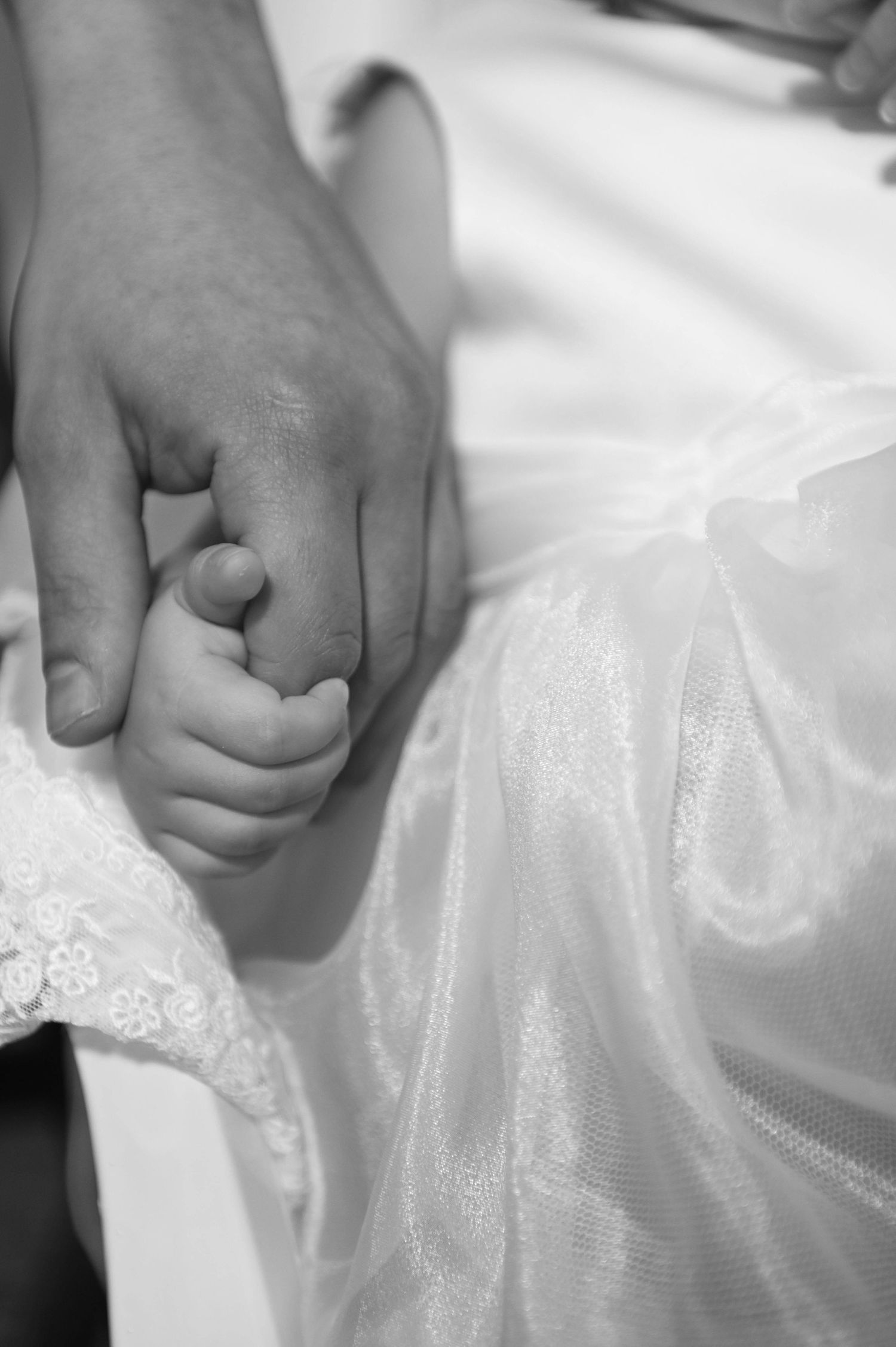 A hand gently holds delicate white lace fabric against a light background in a romantic bridal detail shot.