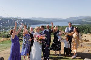 A wedding celebration with confetti toss taking place on a mountaintop overlooking a scenic valley and lake.