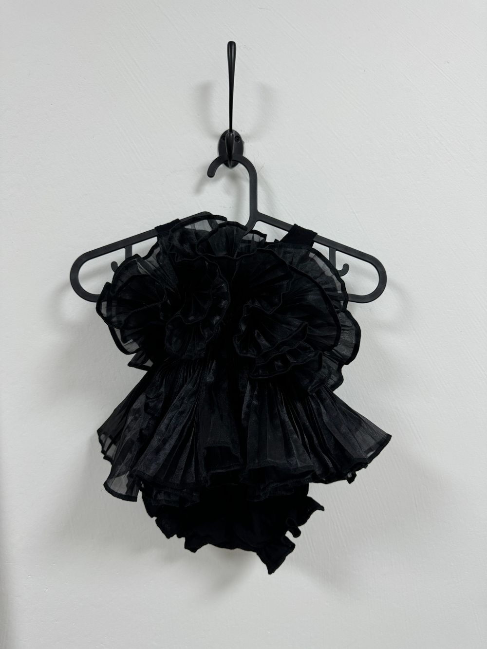 A black ruffled tutu-style dance outfit with layers of tulle fabric hanging on a plastic hanger against a white wall.