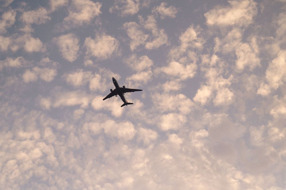 Silhouette of a commercial airliner flying against a cloudy sunset sky with scattered altocumulus clouds.