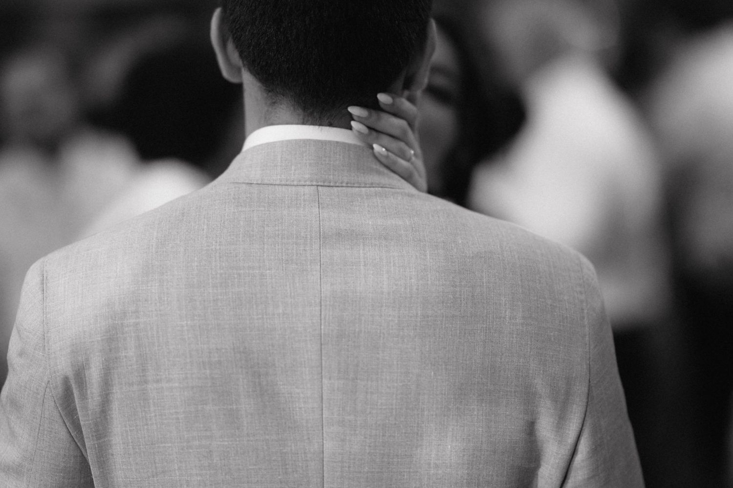 A black and white photo shows the back of someone's head and shoulders wearing a light colored suit jacket.