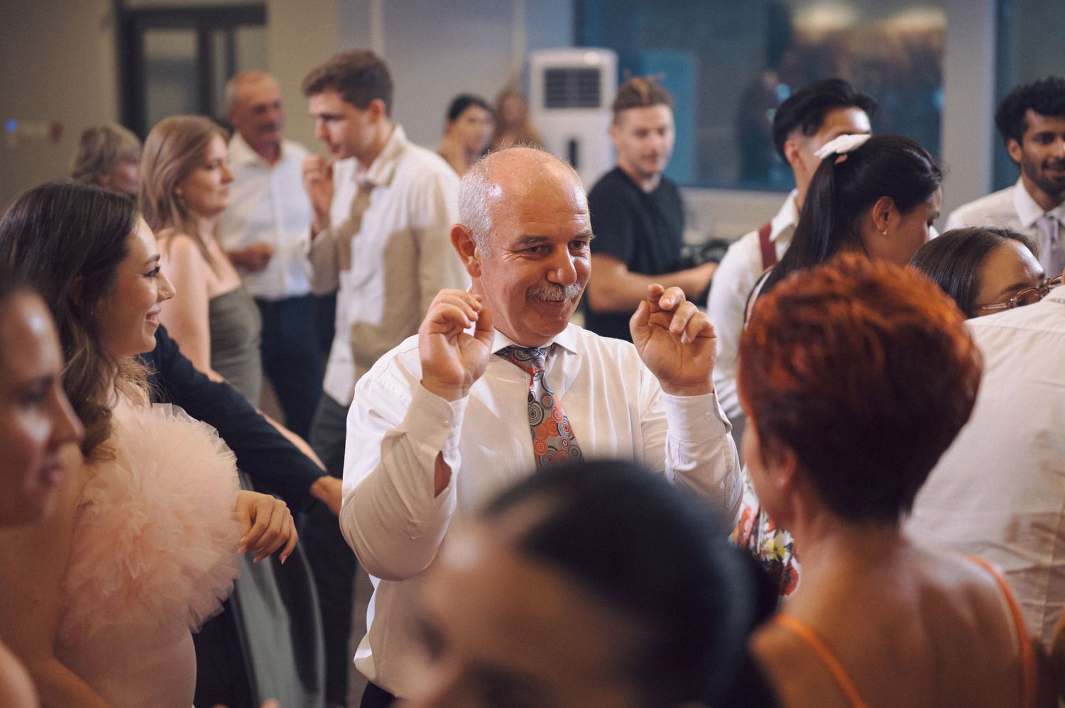 Guests at a wedding reception dance and celebrate on a crowded dance floor.