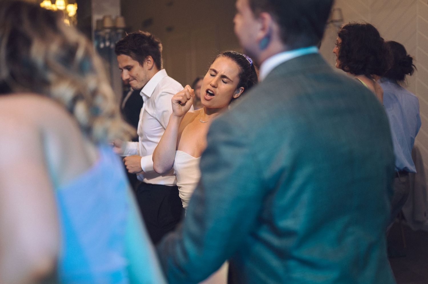 Wedding reception guests dancing and celebrating in a dimly lit indoor venue.