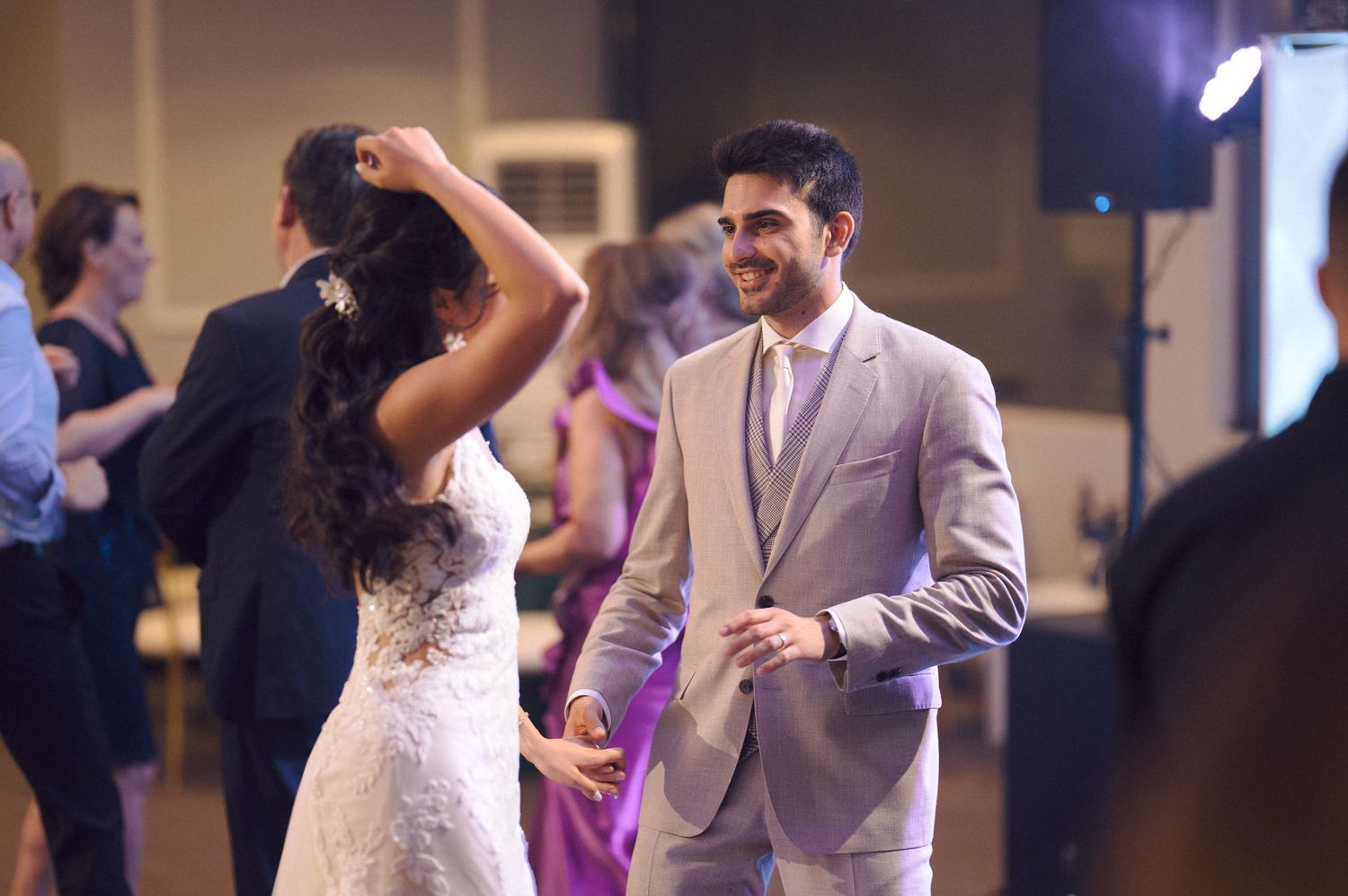 Wedding guests dance and celebrate during a lively reception party with purple lighting in the background.