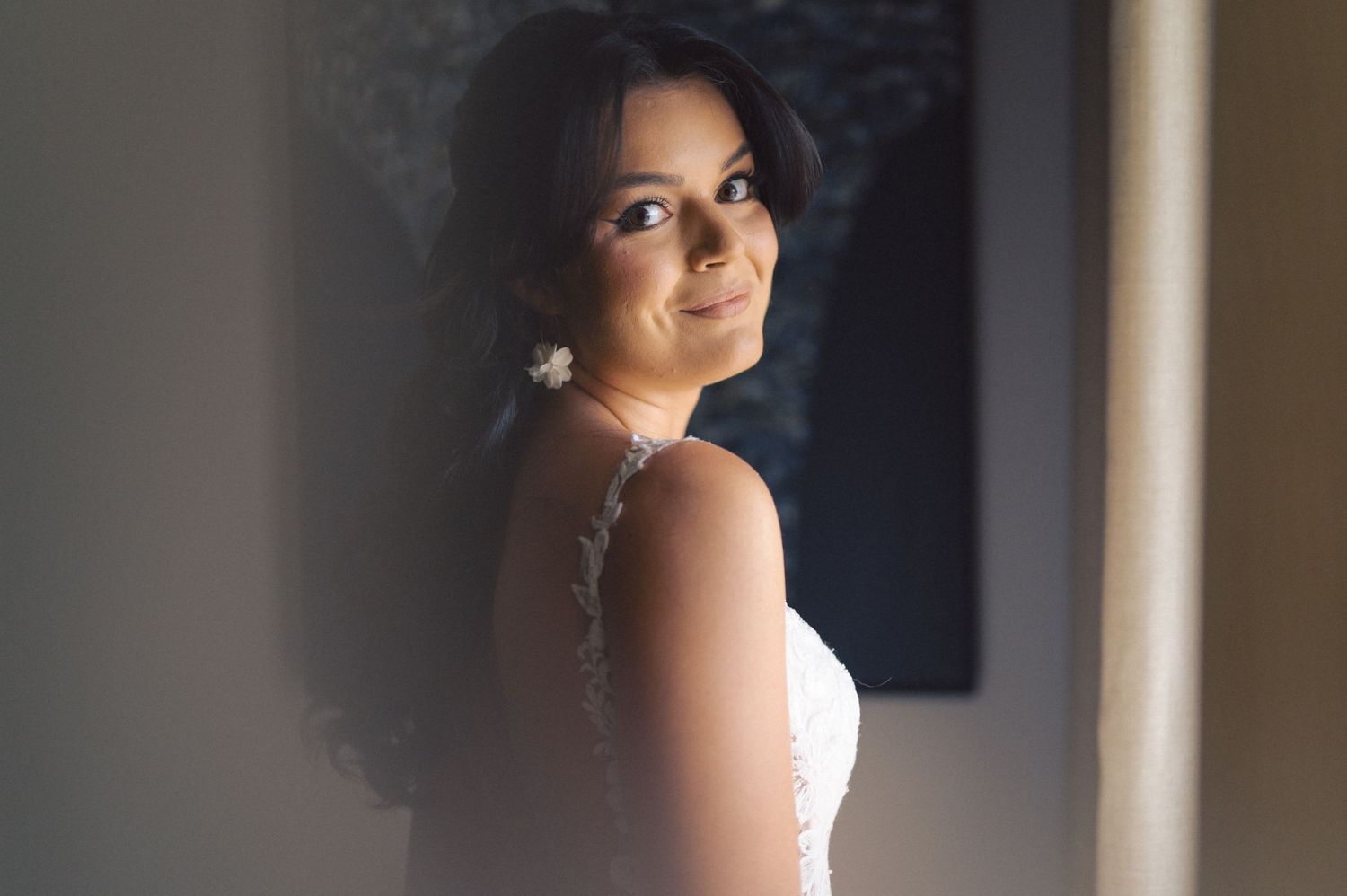 Soft portrait capturing an elegant look over the shoulder in warm lighting with pearl earrings and natural makeup.