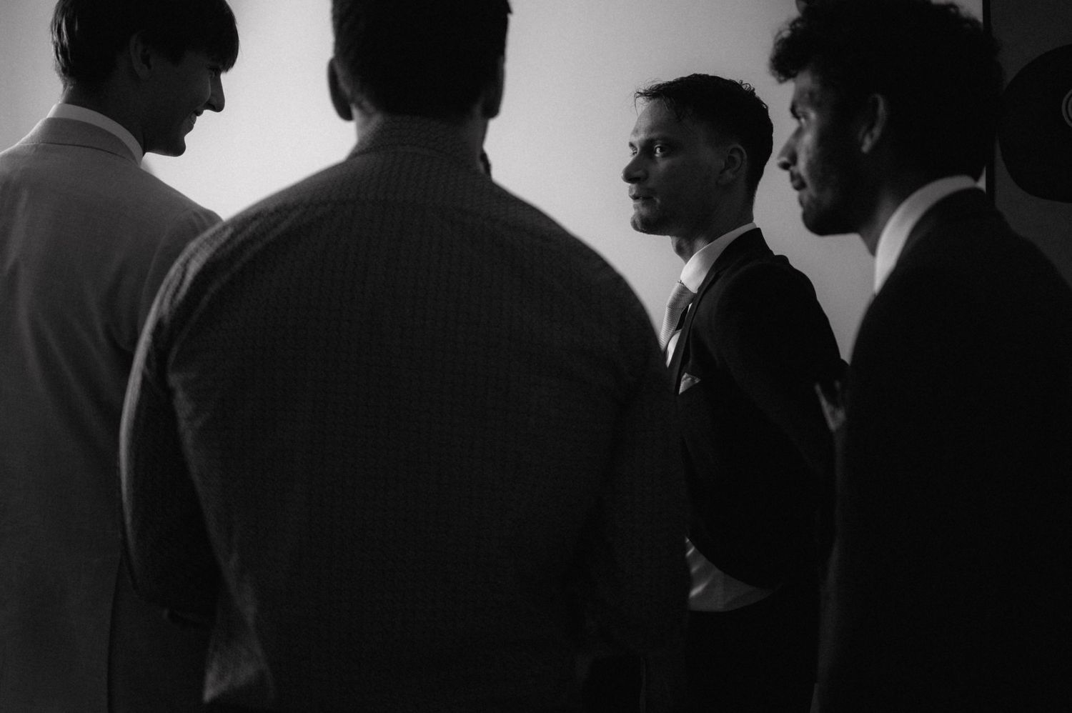 A monochrome photograph showing silhouettes of men in suits having a conversation in dramatic side lighting.