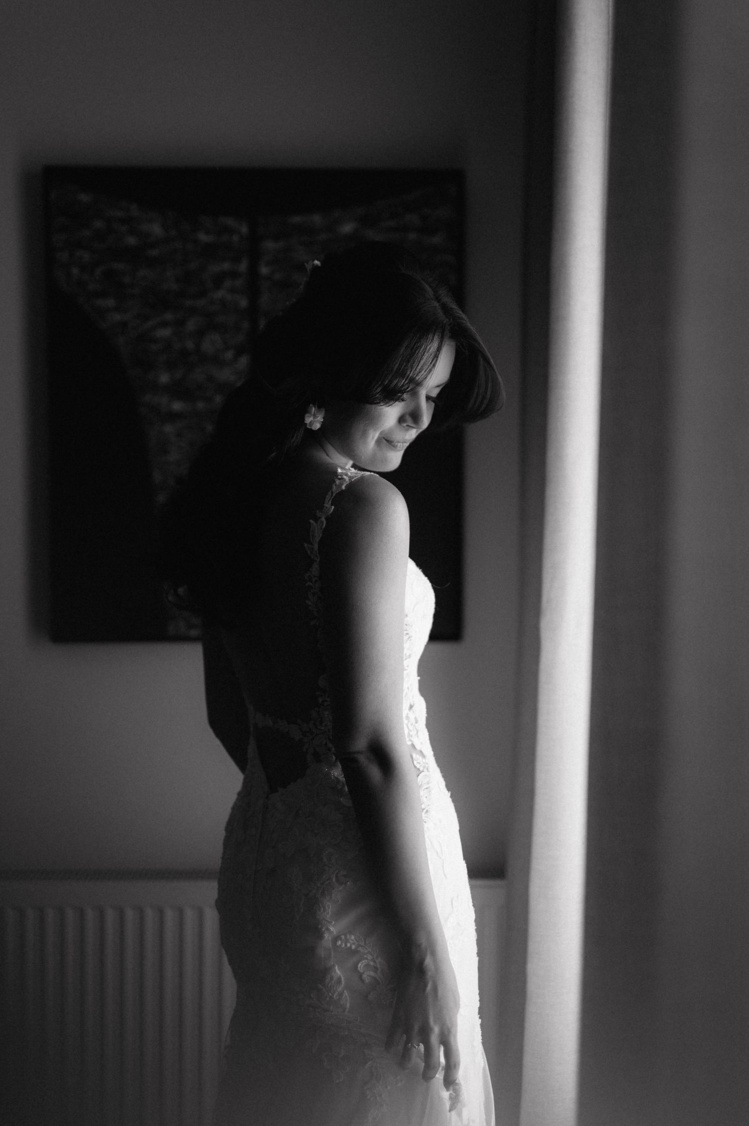 Artistic black and white photograph of a pregnant woman in a white dress standing in front of a window.
