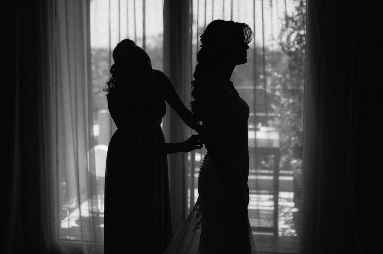 Black and white silhouette of two people standing near a window, creating a dramatic and moody atmosphere.