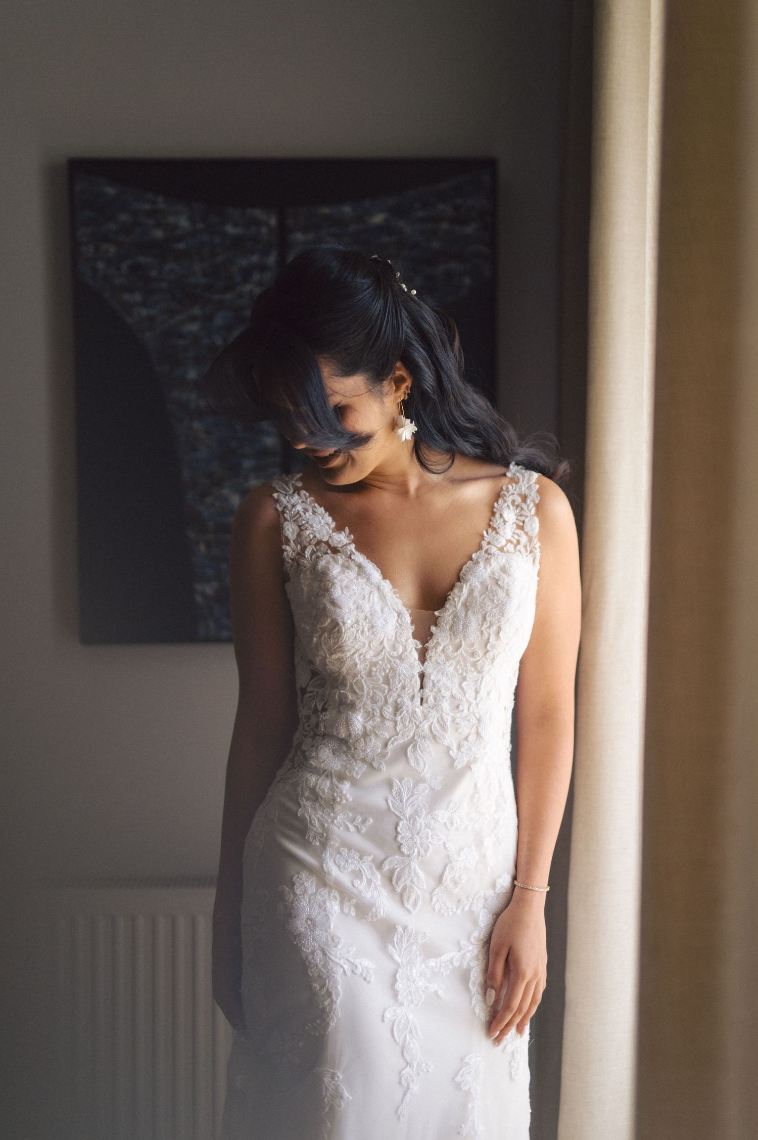 A detailed white lace wedding gown with deep v-neckline and intricate embroidery details is captured in soft window light.