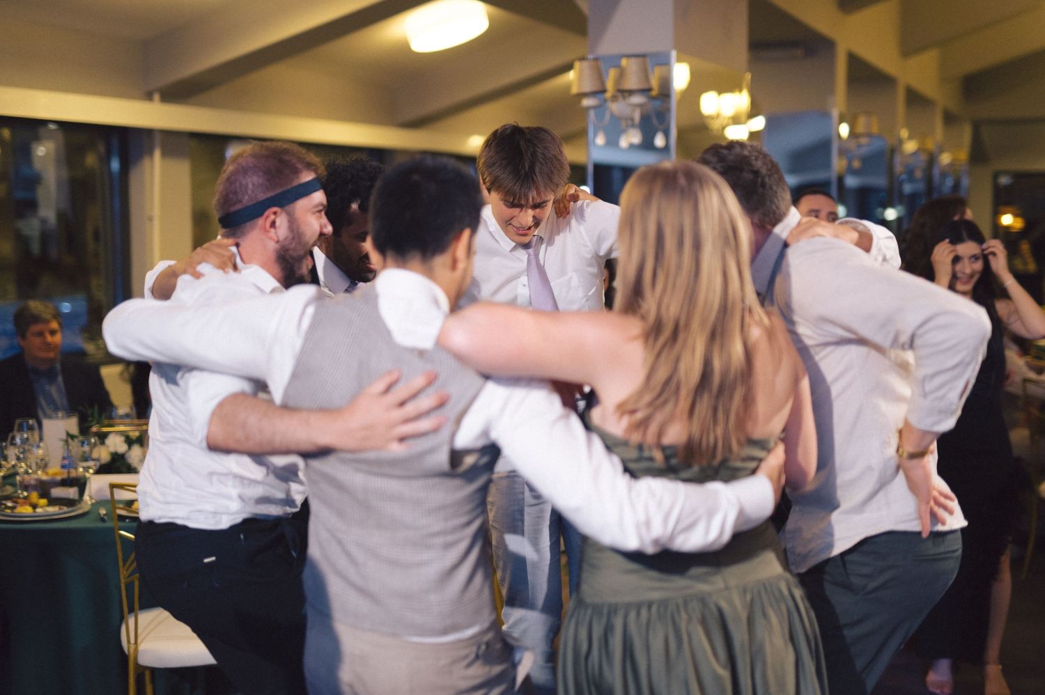 People dancing in pairs at a wedding celebration in an indoor venue with overhead lighting.
