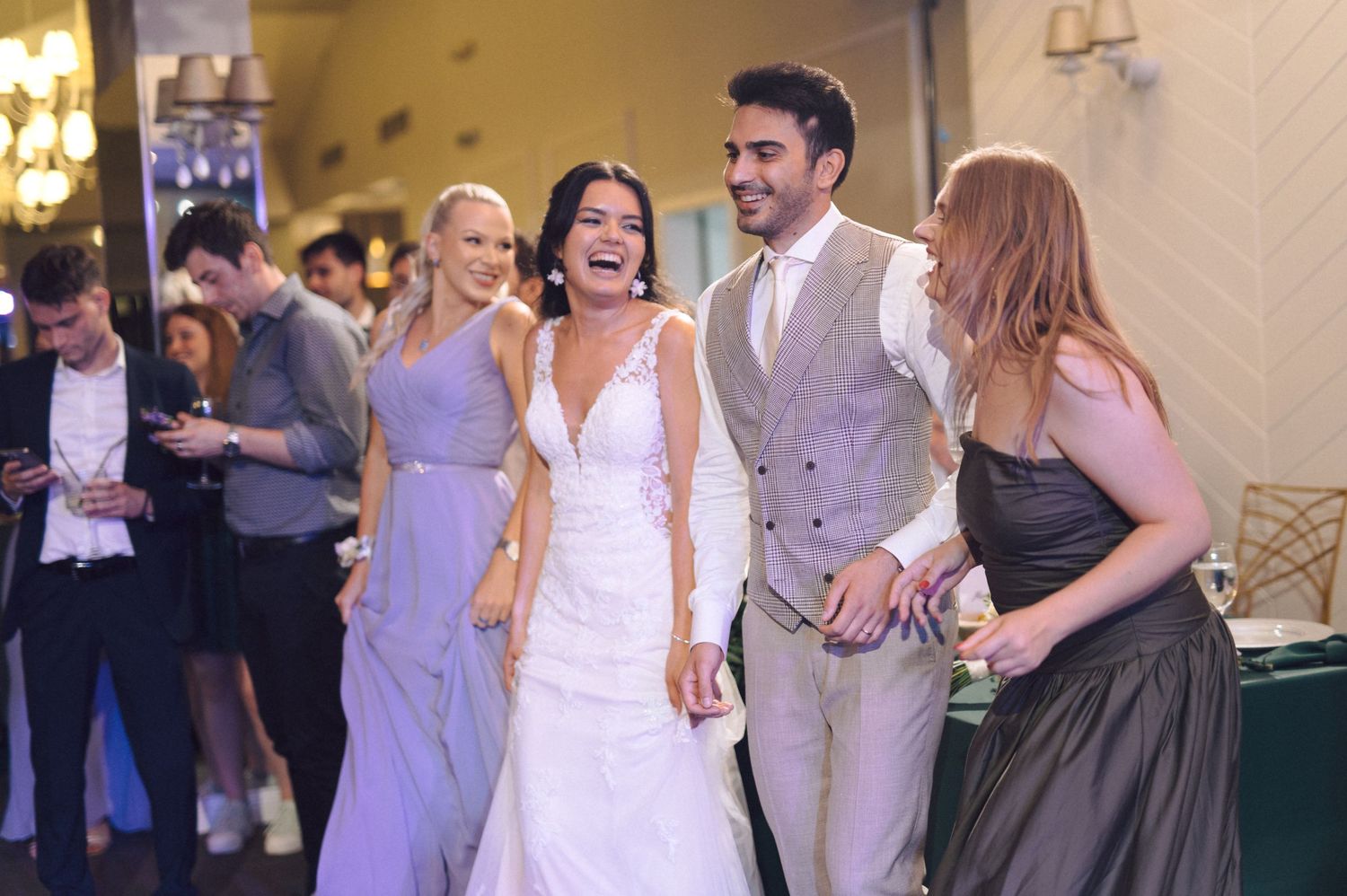 Wedding guests dancing and socializing in an elegantly lit indoor reception venue.