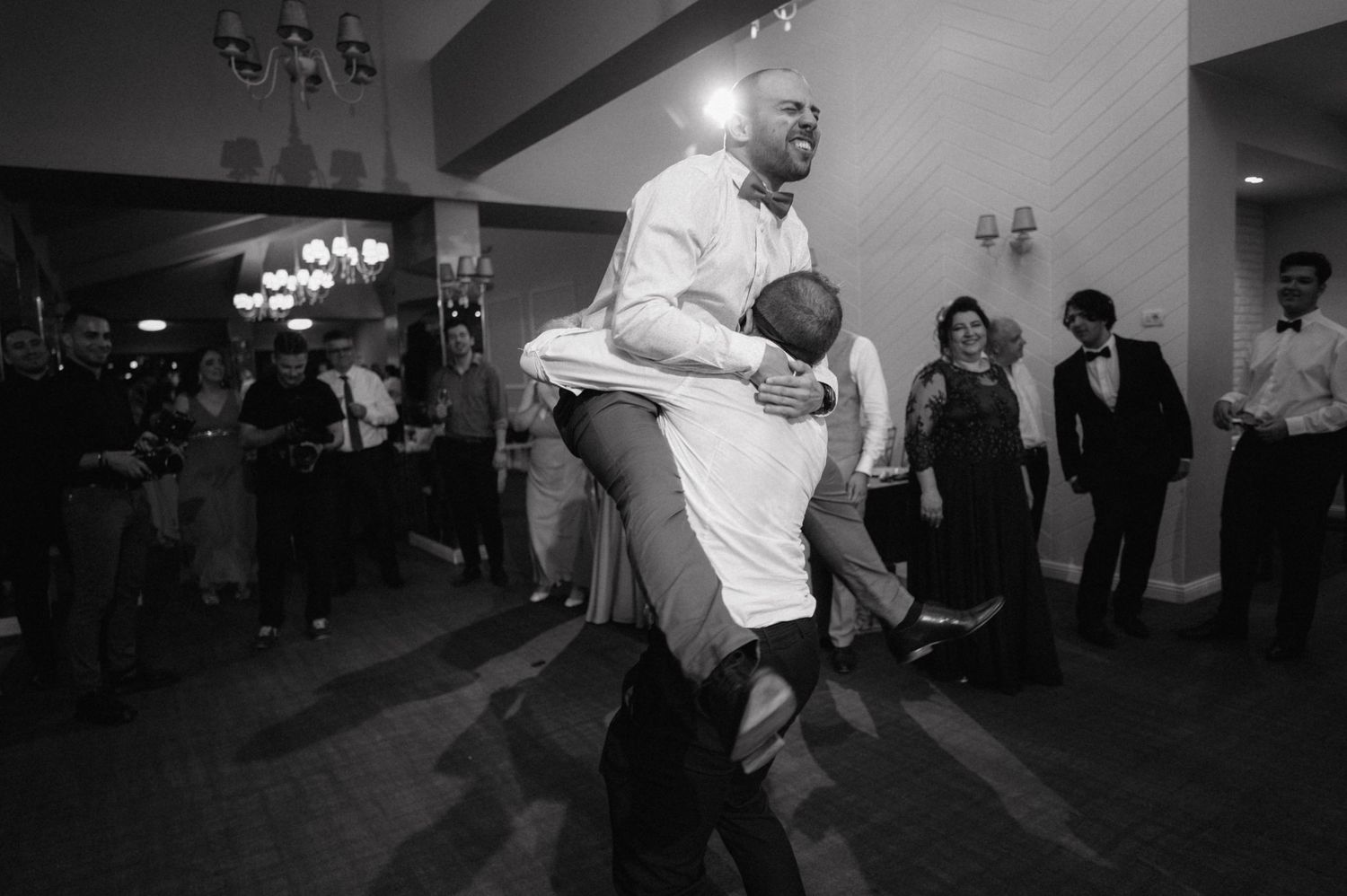 Black and white photo of couples dancing at a formal reception in a chandelier-lit venue.