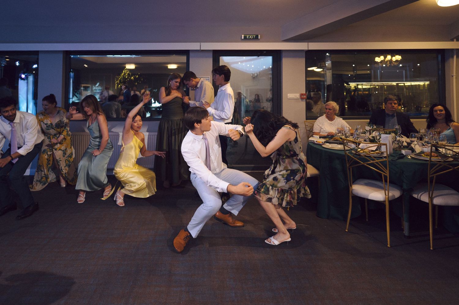 Dancers perform lively swing moves on the dance floor at a formal event with dining tables in the background.