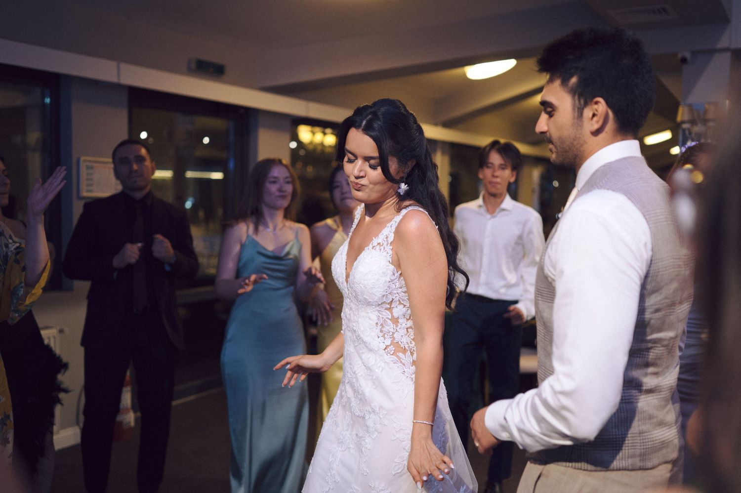 Wedding couple performs their first dance together while family and friends look on during an indoor reception.