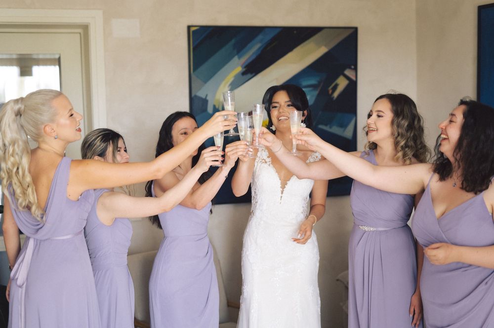 Bridesmaids in lavender dresses share celebratory moments getting ready before a wedding ceremony.
