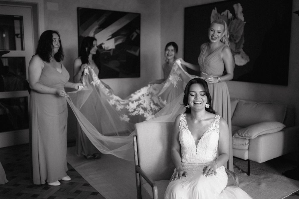 A classic black and white wedding preparation scene shows final dress adjustments in an elegant room.