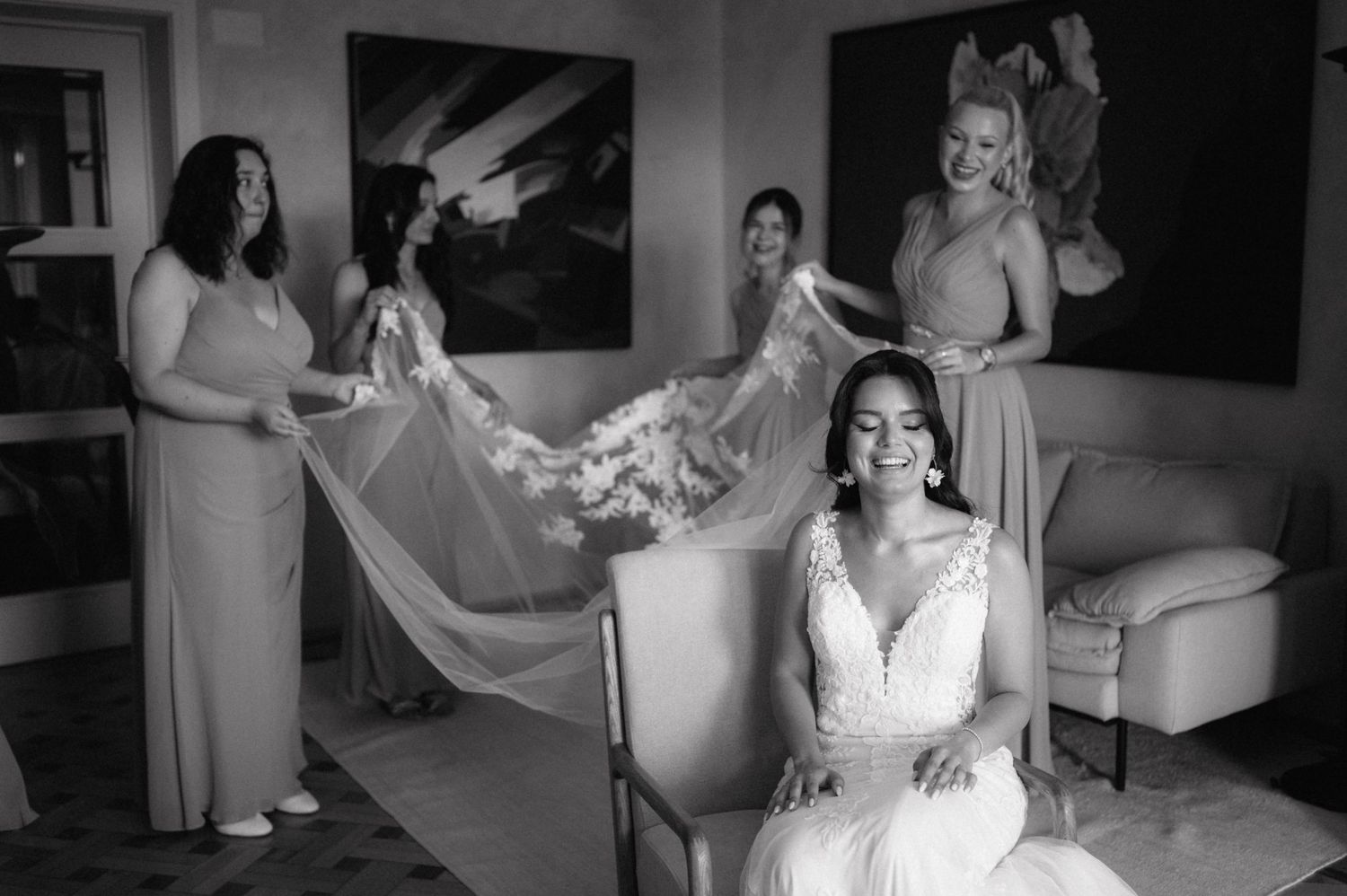 A classic black and white wedding preparation scene shows final dress adjustments in an elegant room.