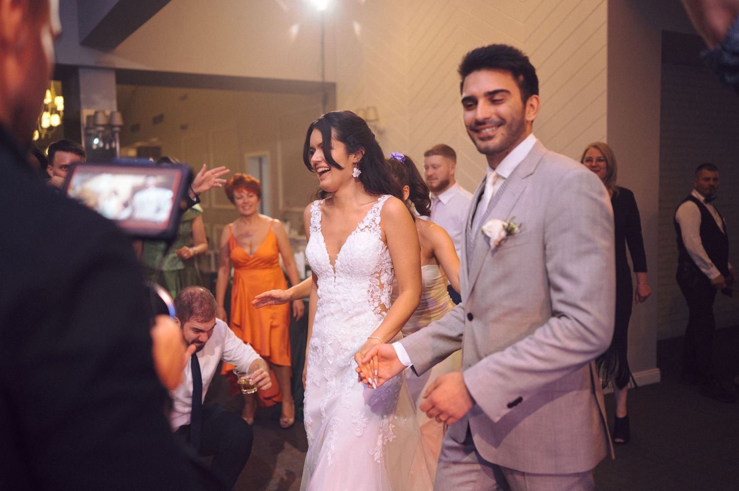 Newlyweds celebrate during their wedding reception with guests looking on in the background.
