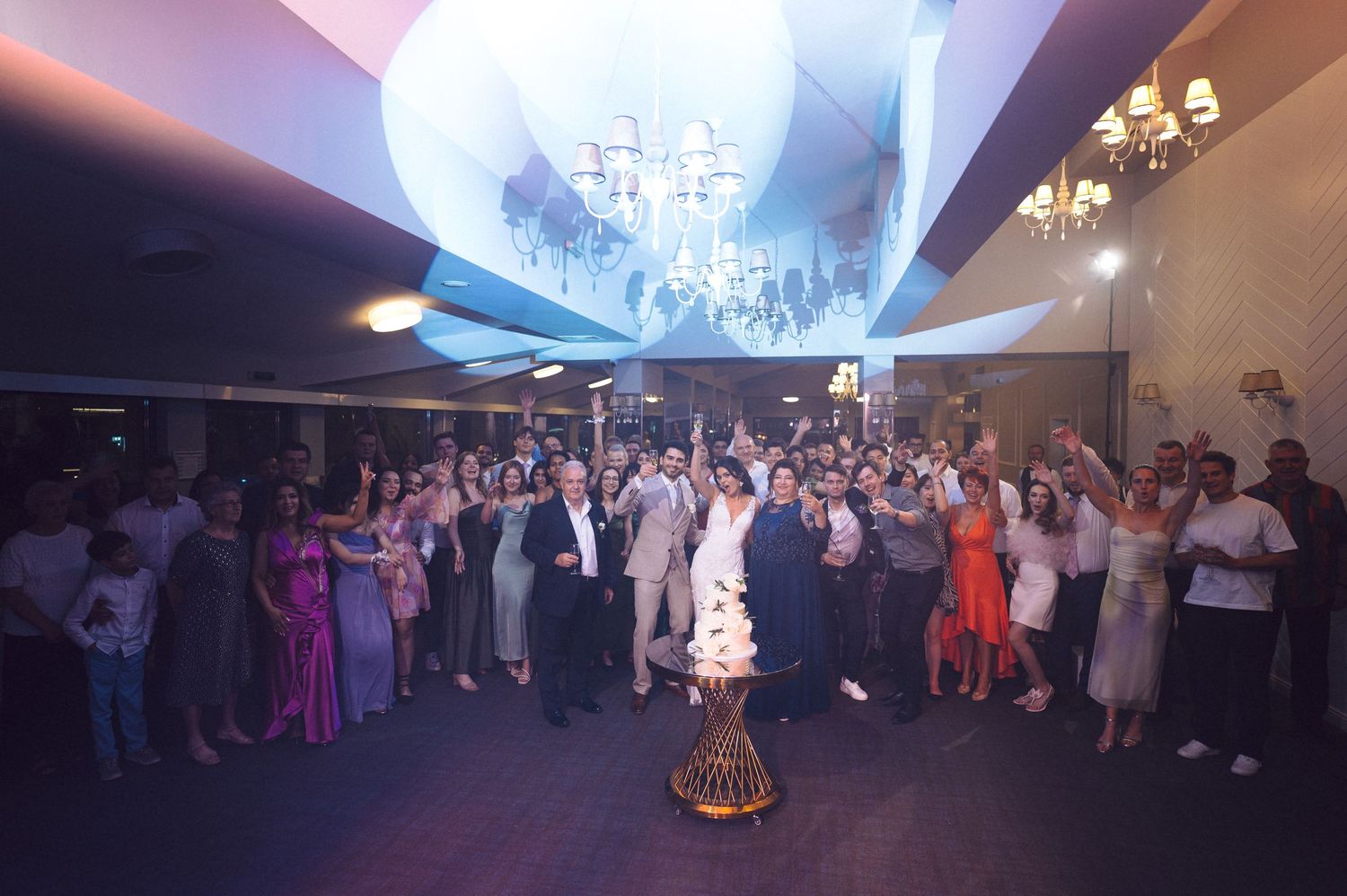 Guests dance beneath a glowing disco ball and chandelier at an elegant formal event in a dimly lit ballroom.