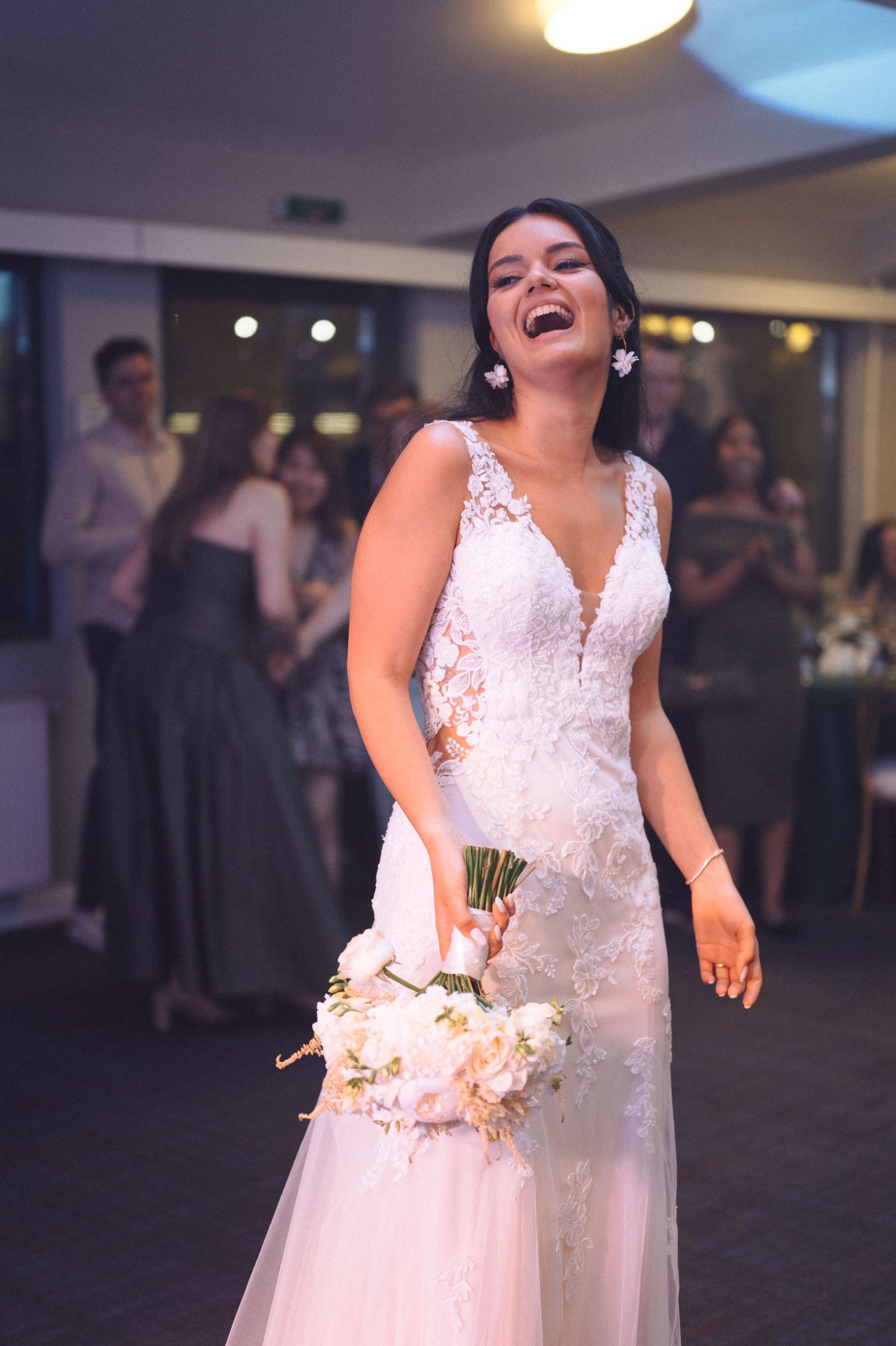 A bride in a white lace dress dances joyfully during a wedding reception at an indoor venue.