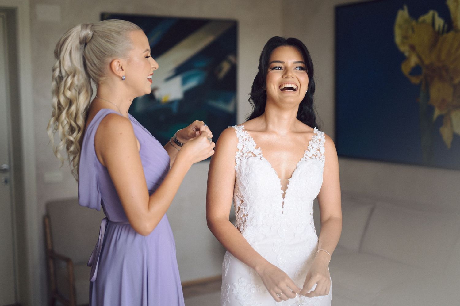 Wedding party members share joyful candid moments in a room with vibrant blue artwork.