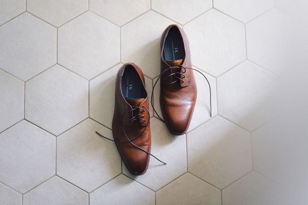 Two brown leather lace-up men's dress shoes arranged in different positions on white hexagonal floor tiles.