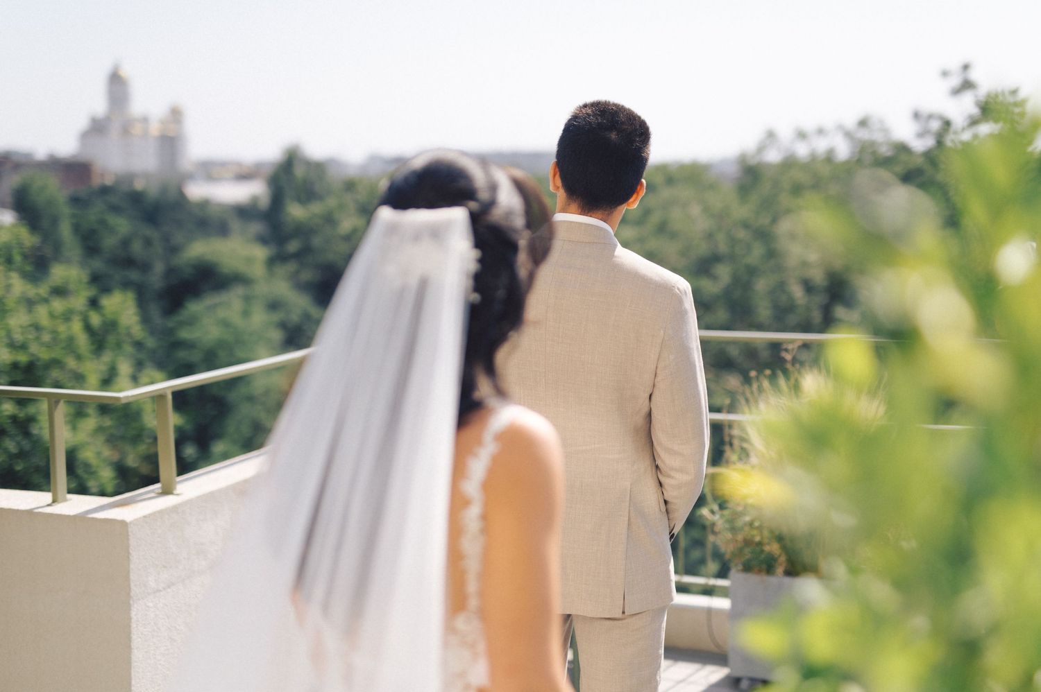 A bride and groom share a first look moment on a balcony with a scenic church view in the background.
