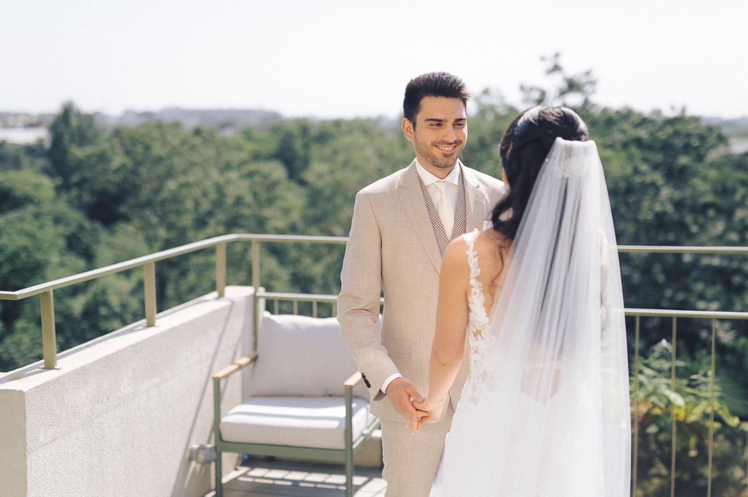 A newlywed couple stands together at an outdoor wedding venue with lush greenery in the background.