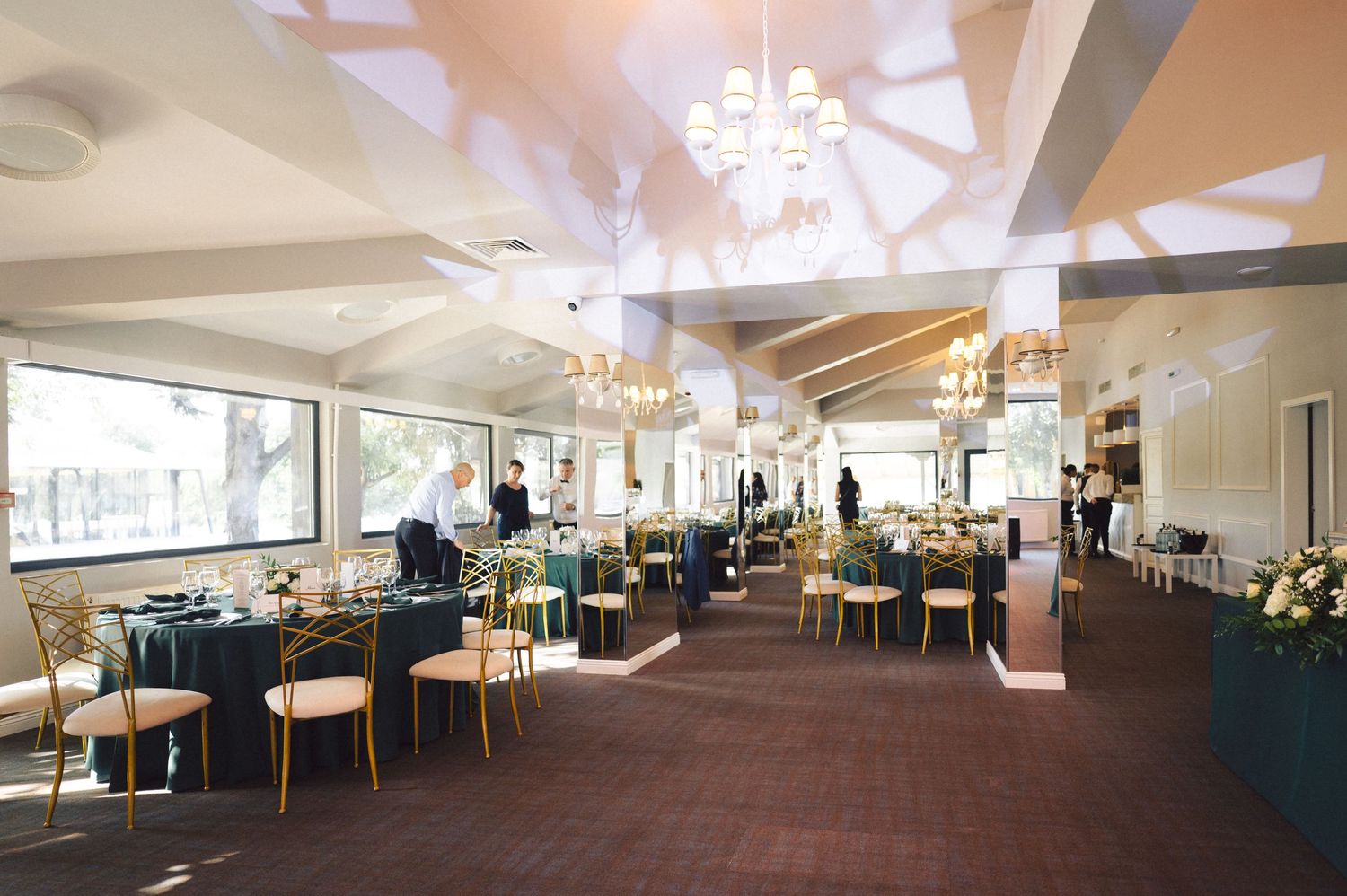 Elegant restaurant interior with teal booths, wooden chairs, and crystal chandeliers in a bright, spacious dining room.
