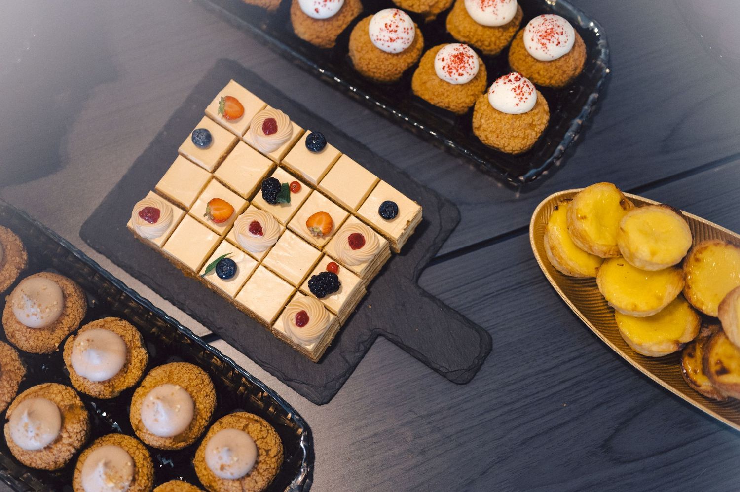 An assortment of elegantly plated petit fours and small desserts arranged on dark serving platters.