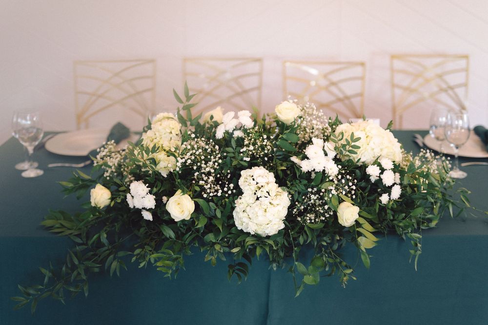 White floral arrangements with greenery line a wedding venue wall creating an elegant overhead display.