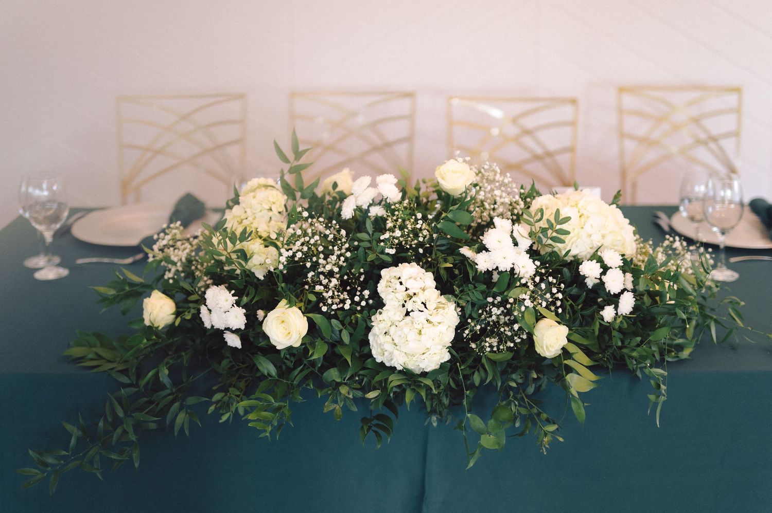 White floral arrangements with greenery line a wedding venue wall creating an elegant overhead display.
