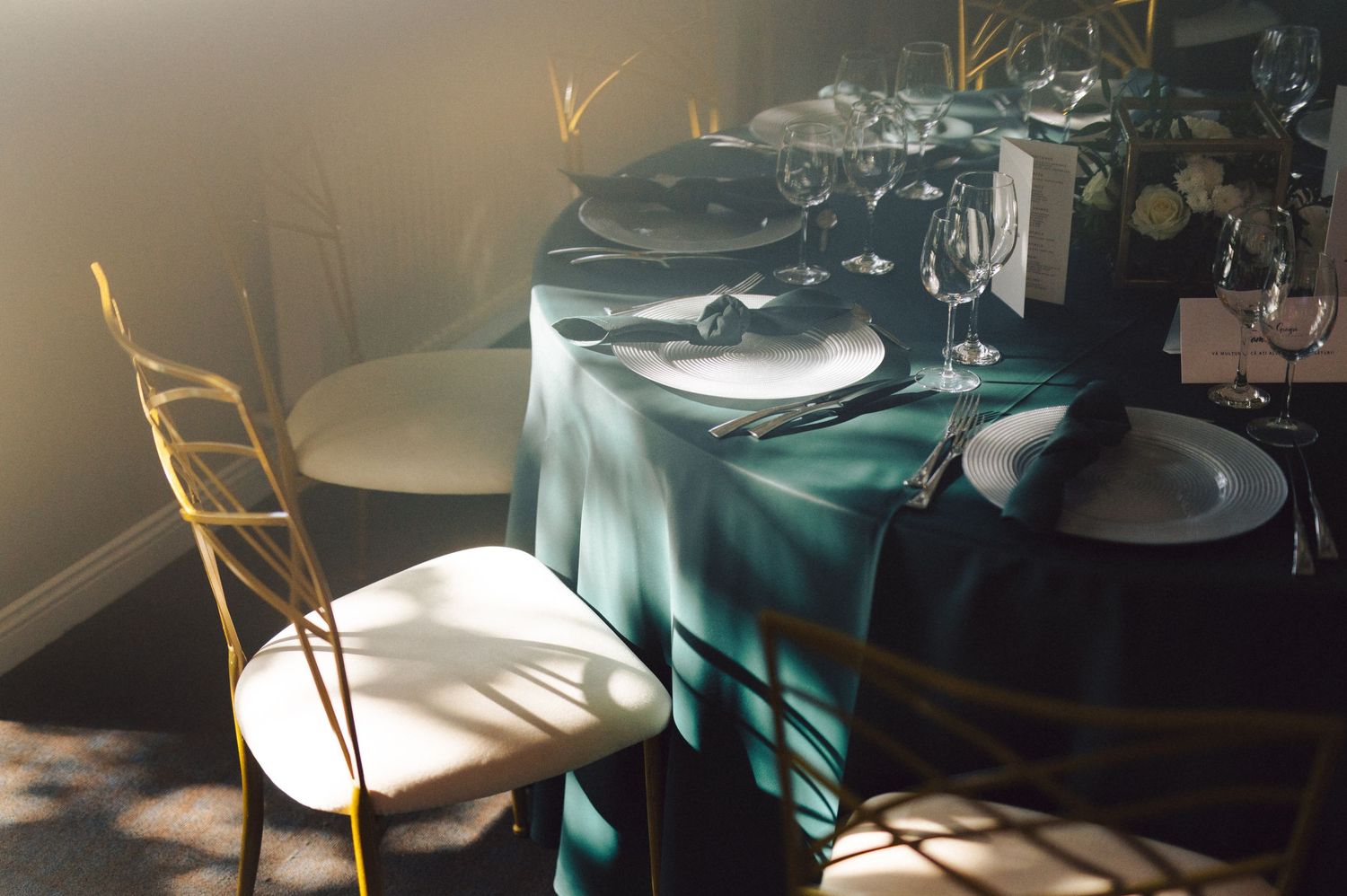 Restaurant dining tables with green tablecloths and gold-colored wooden chairs arranged in an elegant interior setting.