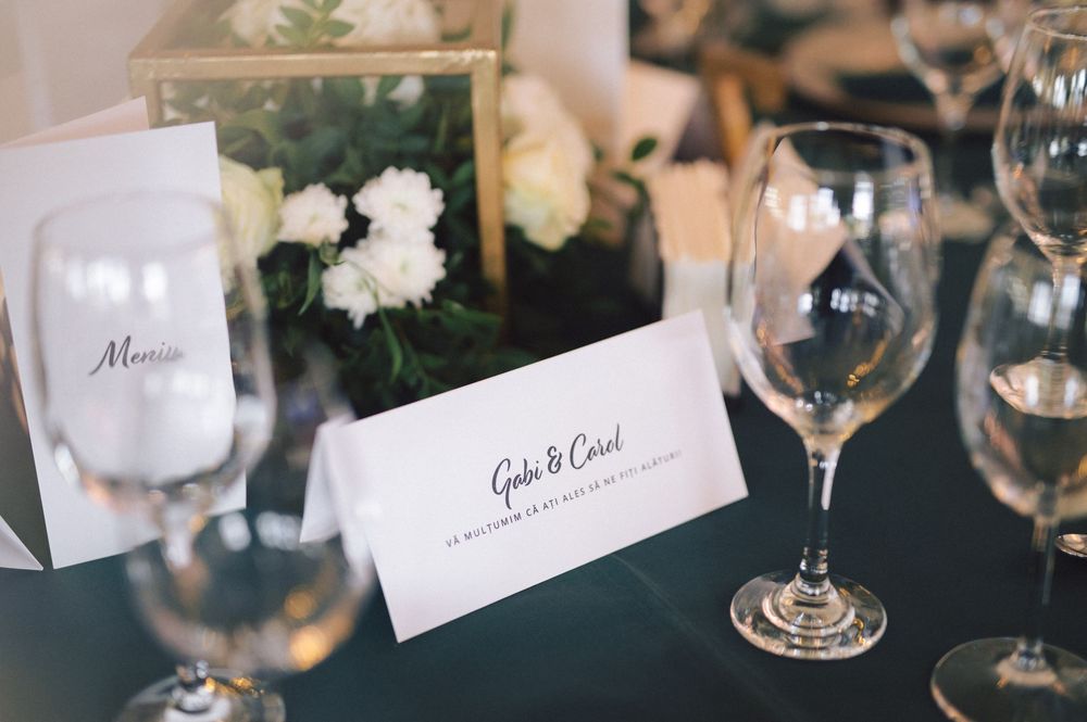 Elegant wedding place setting with menu card, white floral arrangement and wine glasses on dark table.
