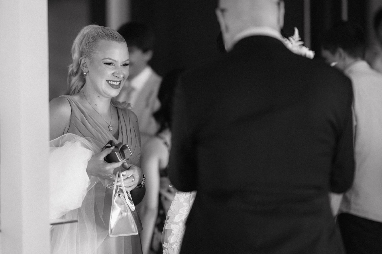 A candid black and white photograph of a joyful wedding guest laughing while wearing a formal dress.