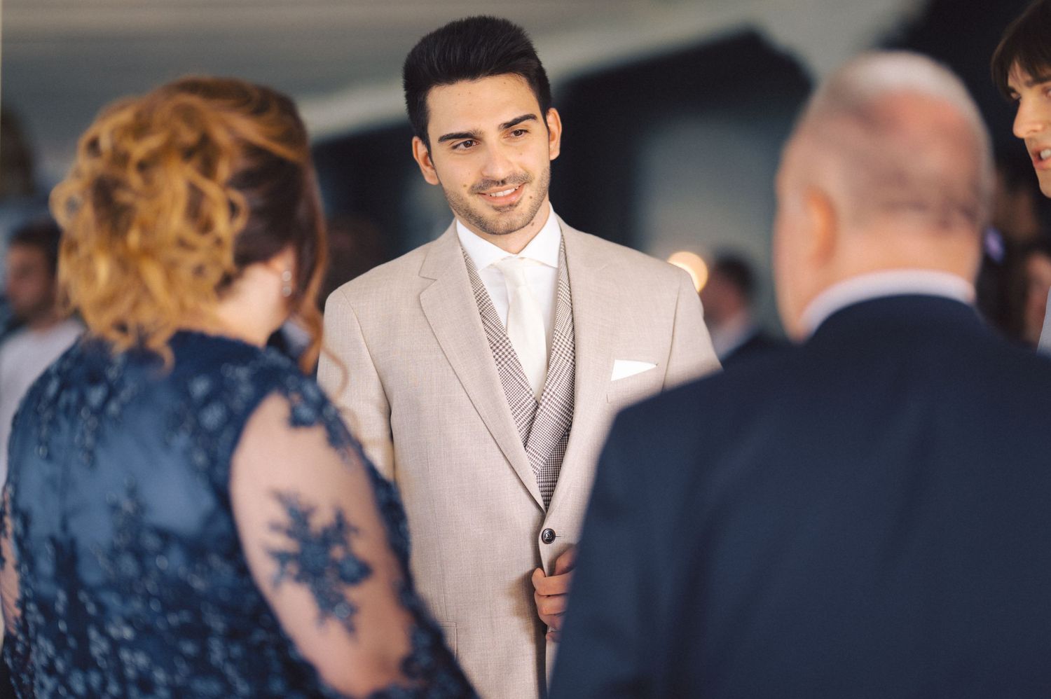 A guest in a light beige suit stands among others during a formal event.