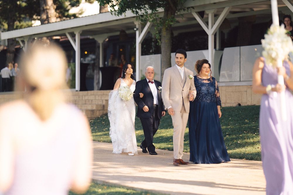 People in formal attire including elegant white and navy blue gowns gather outdoors at a special event.
