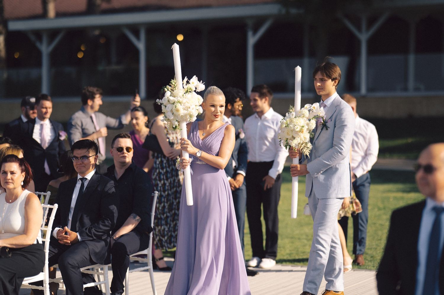 Outdoor wedding ceremony in progress with bridesmaids in lavender dresses and groomsmen in light grey suits.