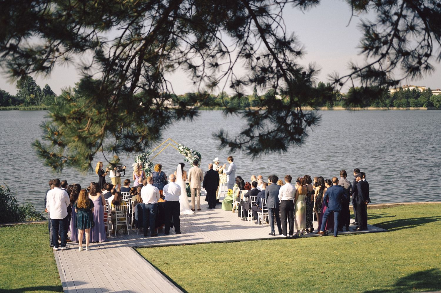 Wedding guests gather by a serene lakeside for an outdoor ceremony at a scenic waterfront location.