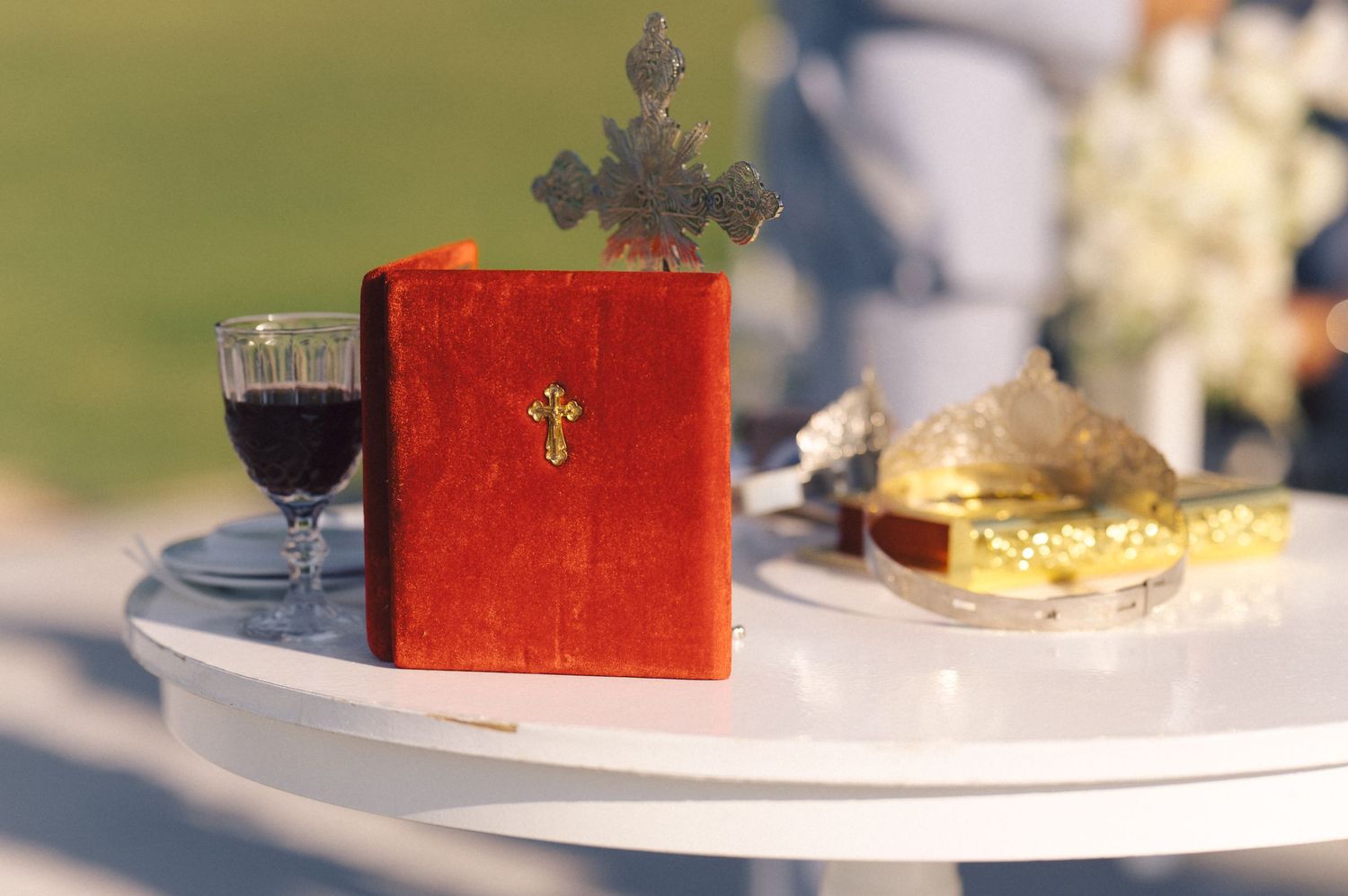 A celebration cake with a metallic gold sheen perched on a pedestal stand with wine glasses in muted lighting.
