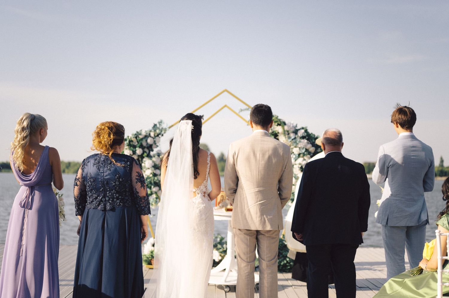 People in formal attire are standing in a line facing away from the camera towards a scenic outdoor view.
