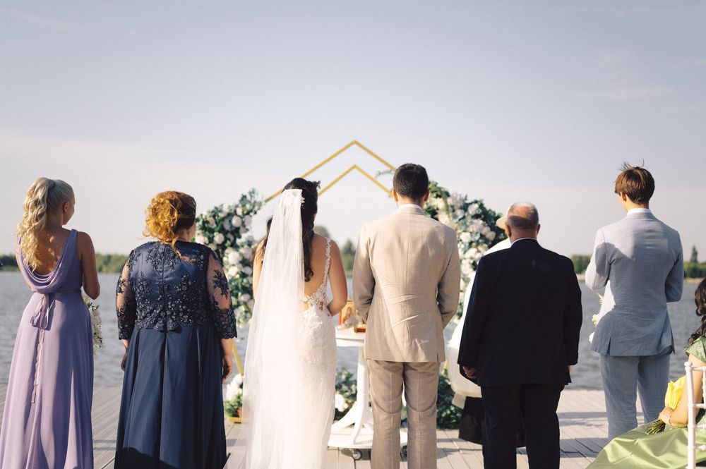 People in formal attire are standing in a line facing away from the camera towards a scenic outdoor view.
