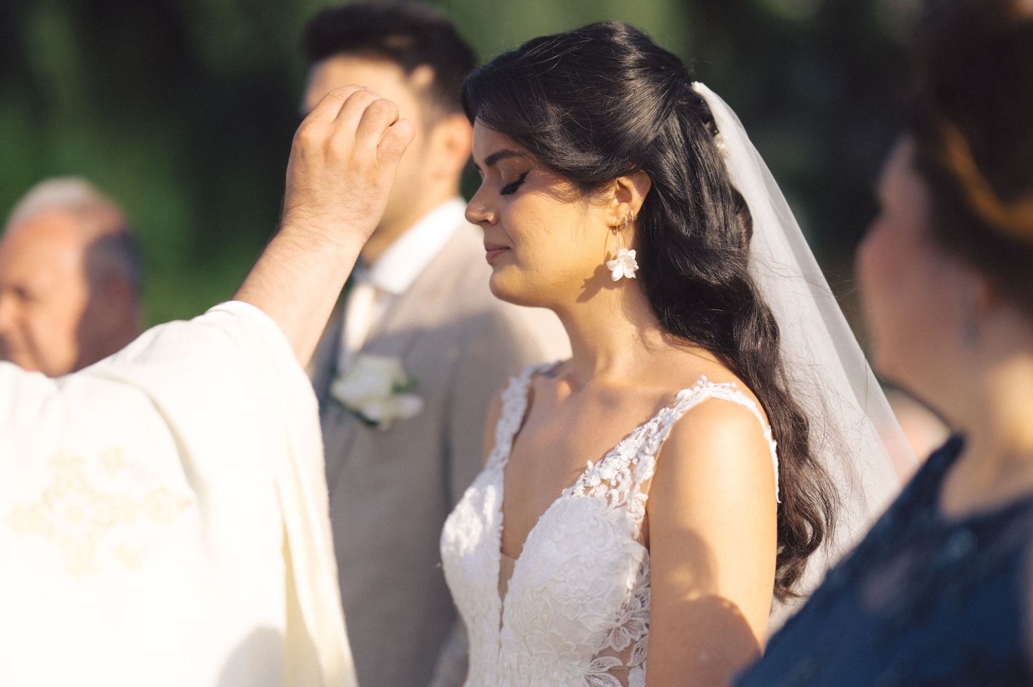 Newlywed couple shares an intimate moment during outdoor wedding ceremony as bride wears lace white gown with veil.